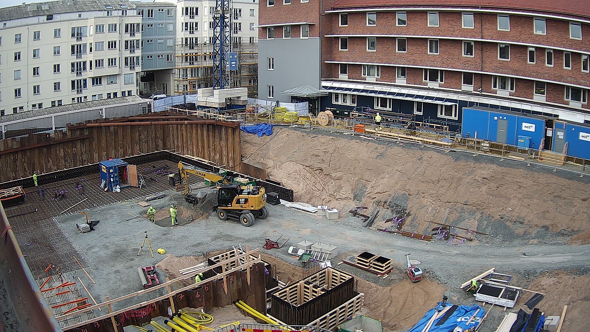 Byggarbetsplatsen sett från hus 01 med nuvarande Science Park House i bakgrunden. En gul grävmaskin är på plats och arbetare är på plats och jobbar.