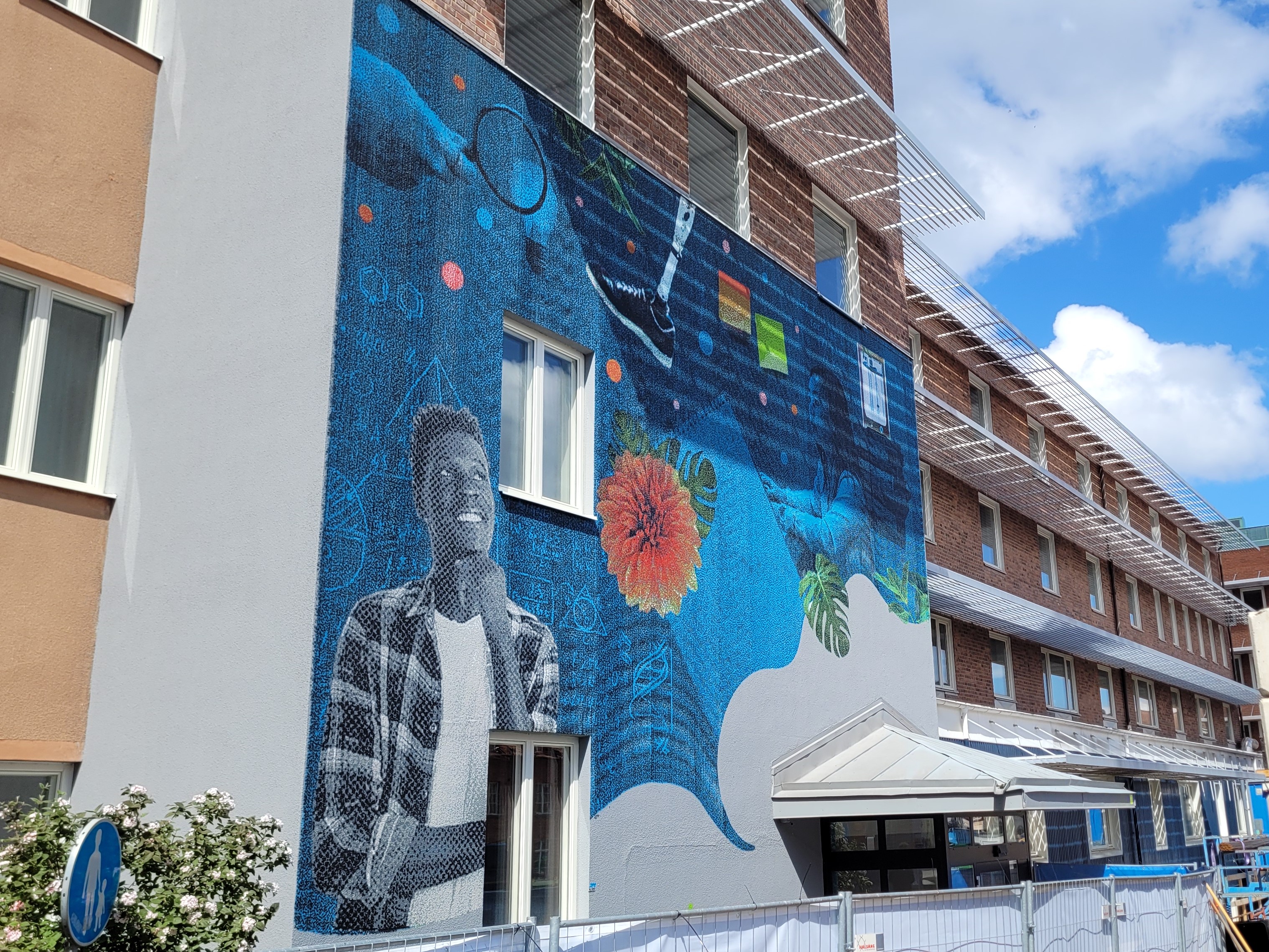 Muralmålningen som målats på Science Parks byggnad. En blå målning med en kille som ler, en gul blomma, posterlappar mm.