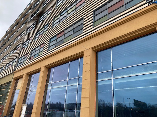 Detaljbild på fasaden, med de stora fönsterpartierna, ockrafärgad putsfasad, coverbricks och färgade glaspartier.